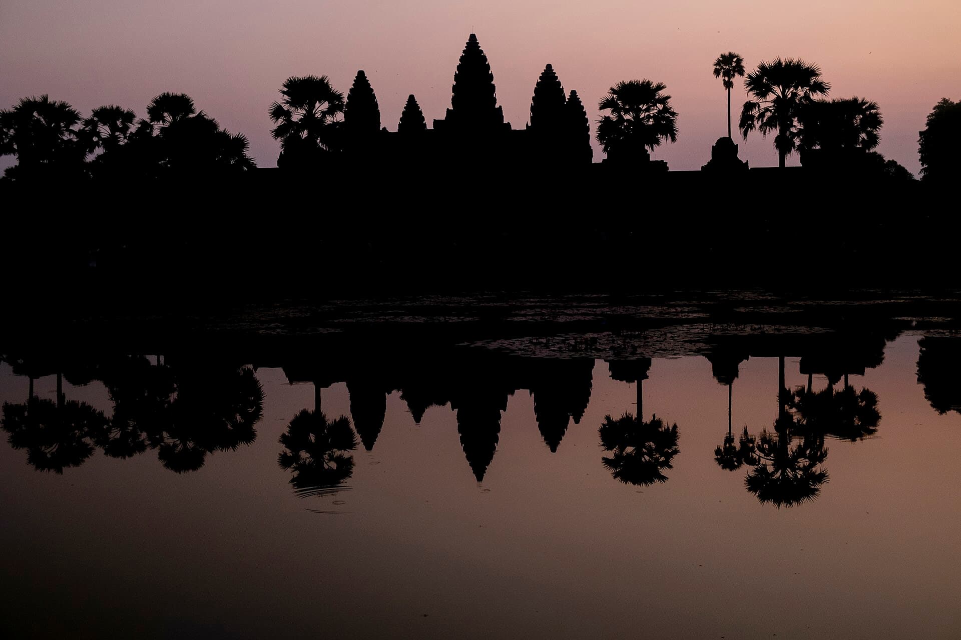 Angkor Wat silhouetted at sunrise, reflected in the water