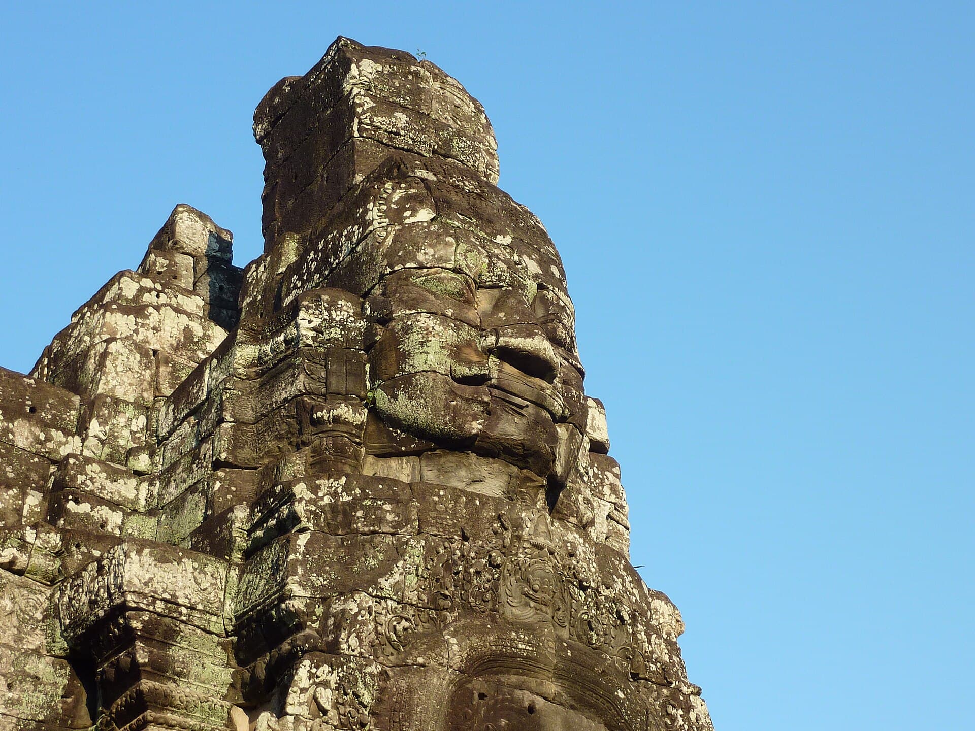 Close-up of a carved stone face on a Bayon tower against a blue sky